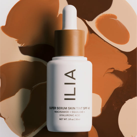 ILIA's Super Serum Skin Tint SPF 40 bottle laid on top of a swirl of different Skin Tint serum shades in the background.