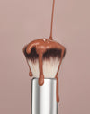 A close up of the Complexion brush with a liquid, complexion product dripping from it.