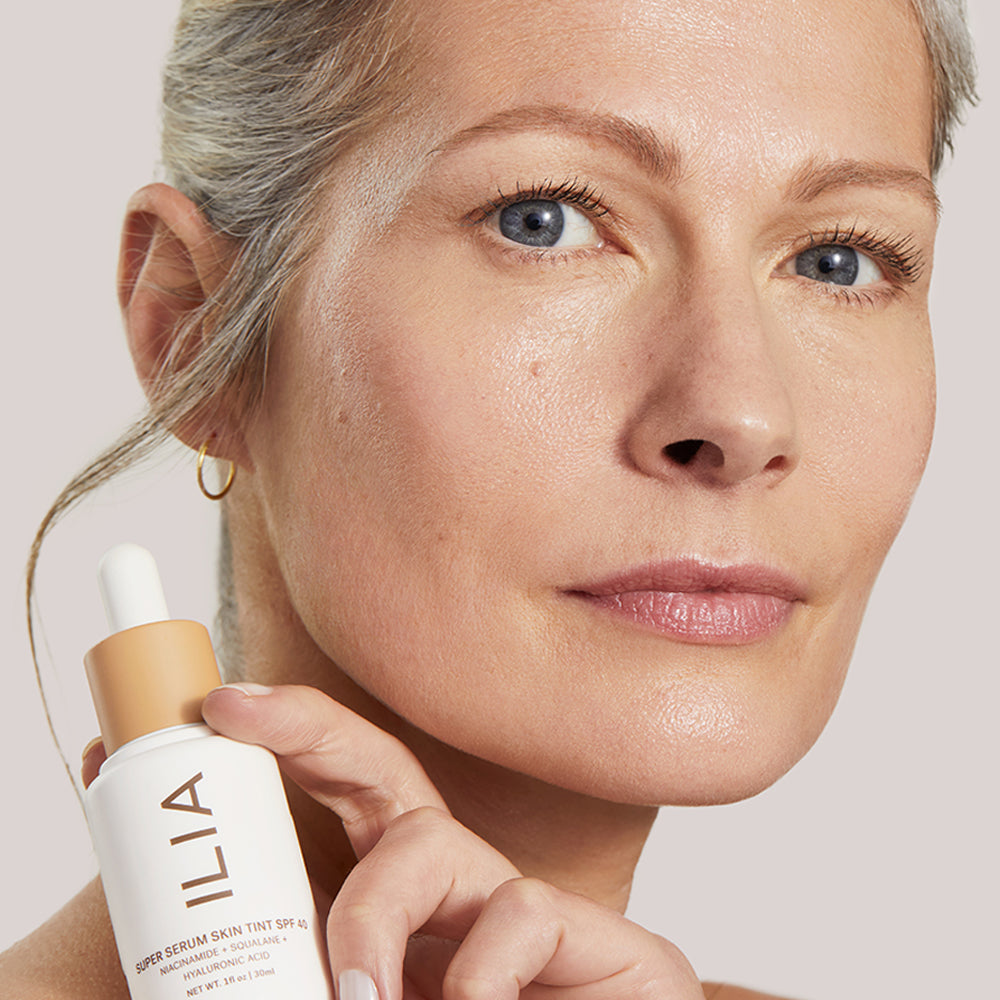 A model with light skin holds ILIA Super Serum Skin Tint SPF 40, showcasing its natural finish.