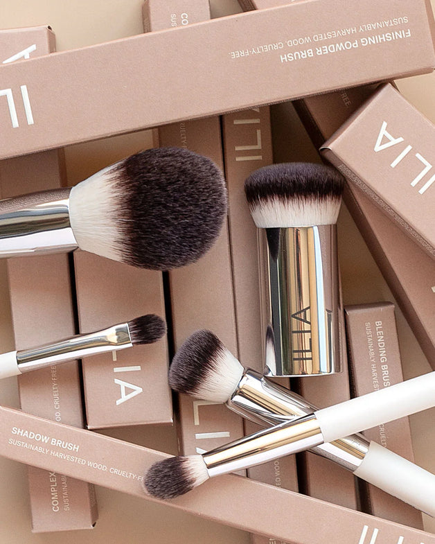 An array of fluffy and dense ILIA brushes laying across ILIA product boxes.