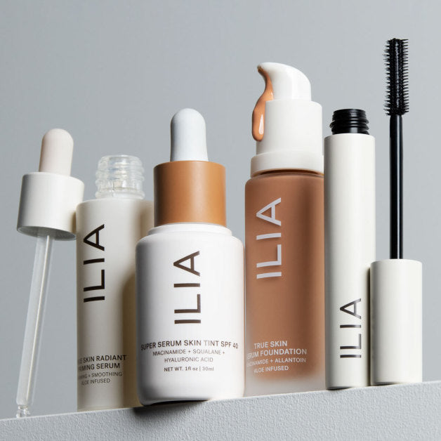 A collection of ILIA Beauty products including serums, foundation, mascara, and skin tint, arranged on a shelf.