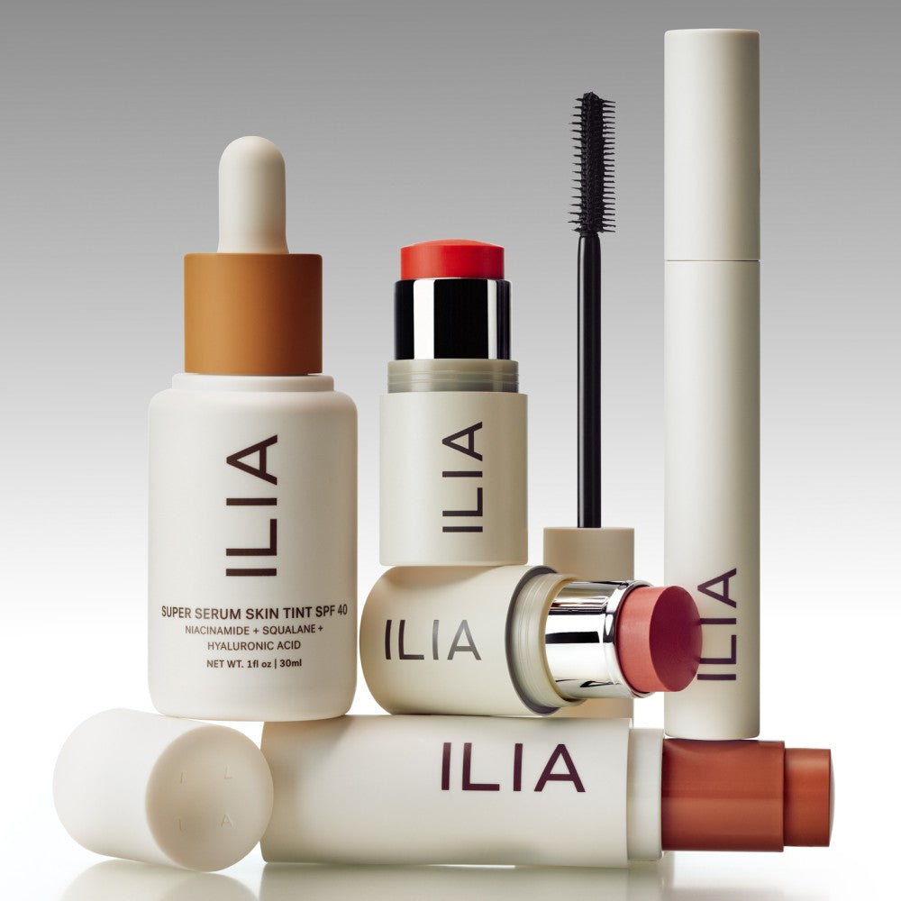 An assortment o ILIA beauty products including Skin Tint, Multi-Sticks, Mascara, and complexion stick.